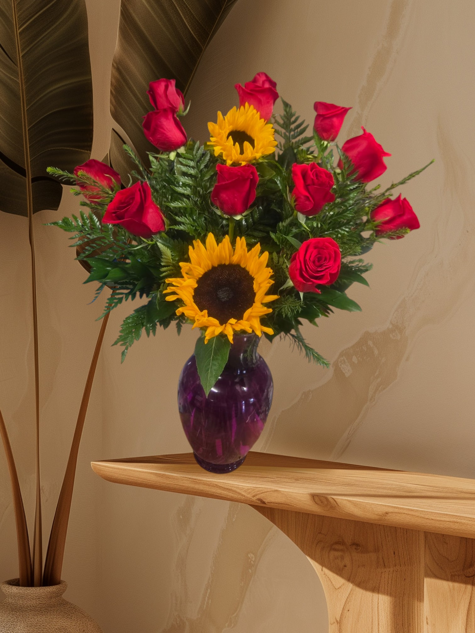 Red roses and sunflowers arranged in a purple glass vase