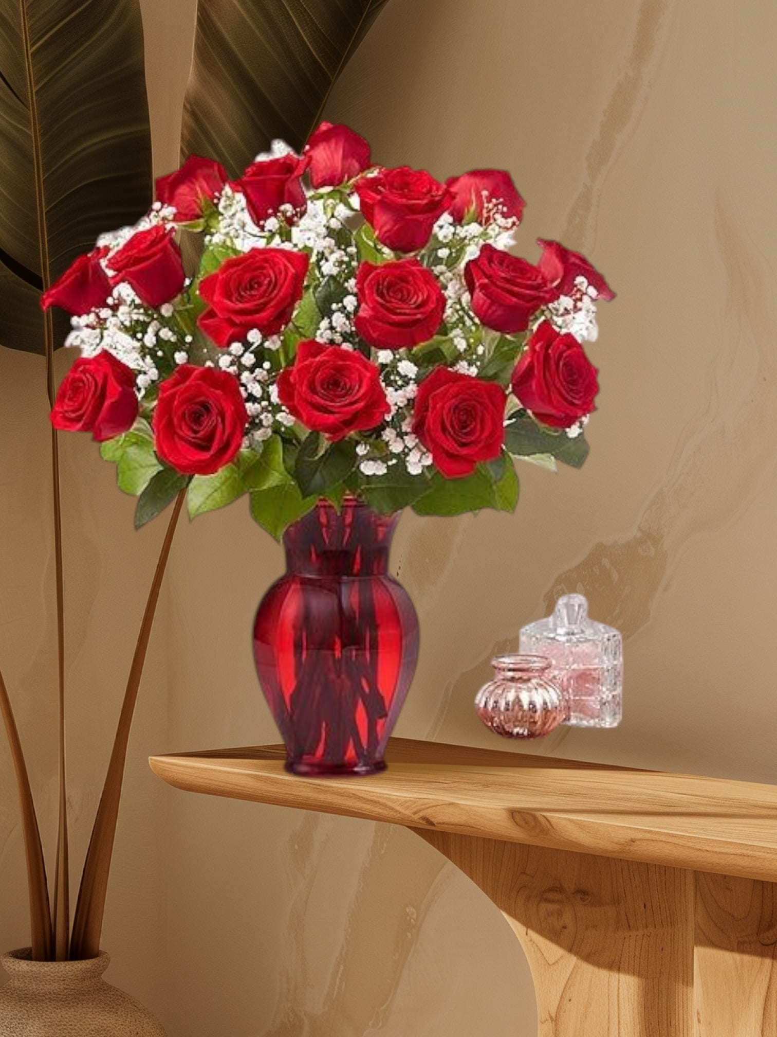 Red roses arranged in a red glass vase with white filler flowers