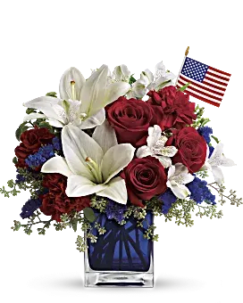The America Beautiful - A patriotic pick to send a brave veteran, decorate your Fourth of July picnic, or celebrate Memorial Day. Lush red, white and blue flowers are presented in a deep blue glass cube vase along with an American flag.