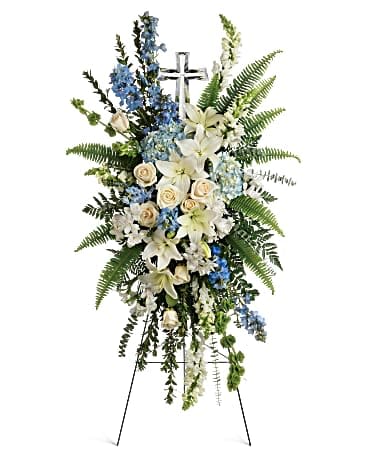 Tall funeral spray of white lilies, cream roses, and blue flowers on an easel
