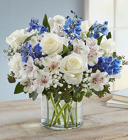 White roses and blue flowers arranged in a clear glass vase