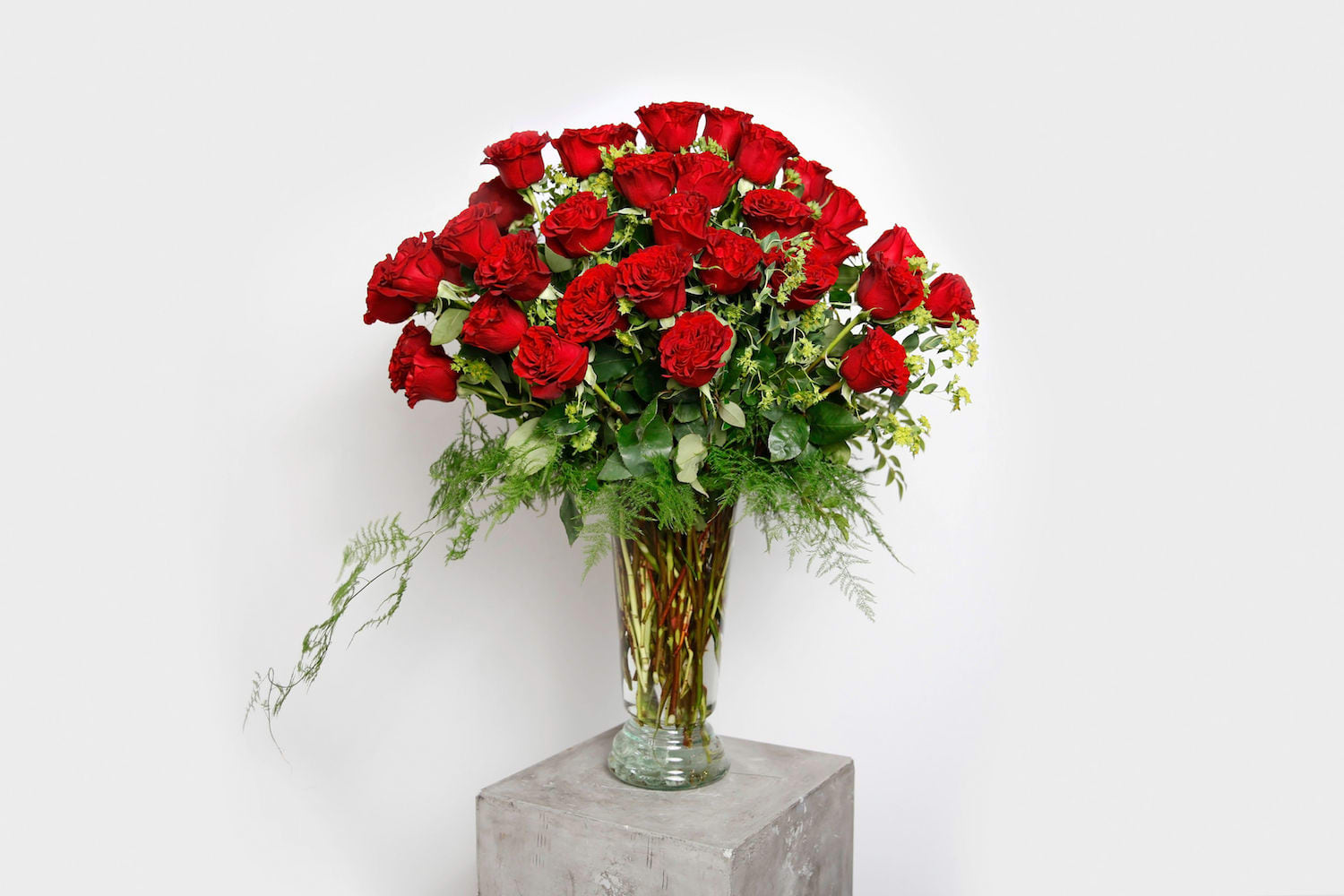 Tall vase arrangement of red roses with greenery