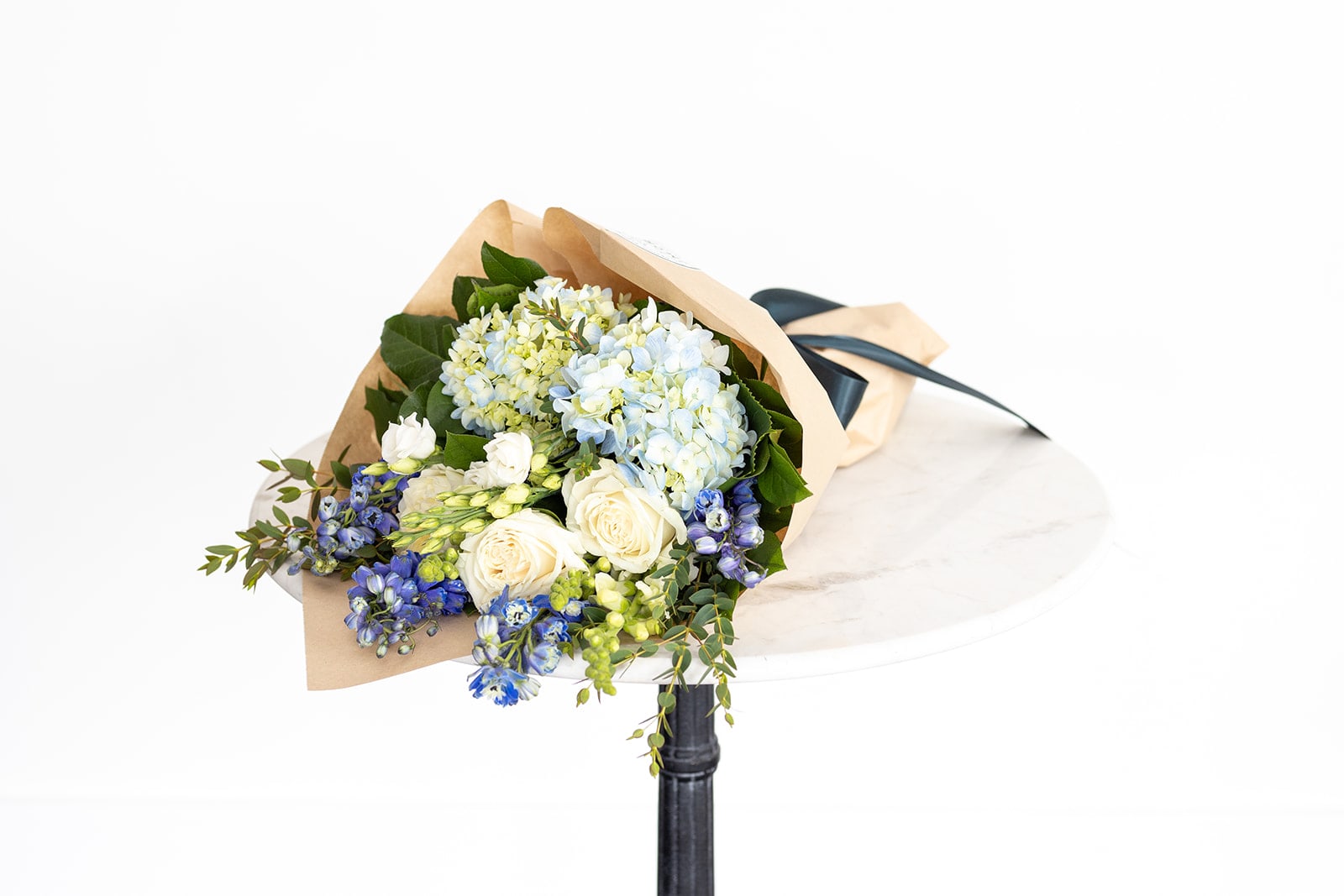 Bouquet of blue hydrangeas, white roses, and blue flowers wrapped in paper