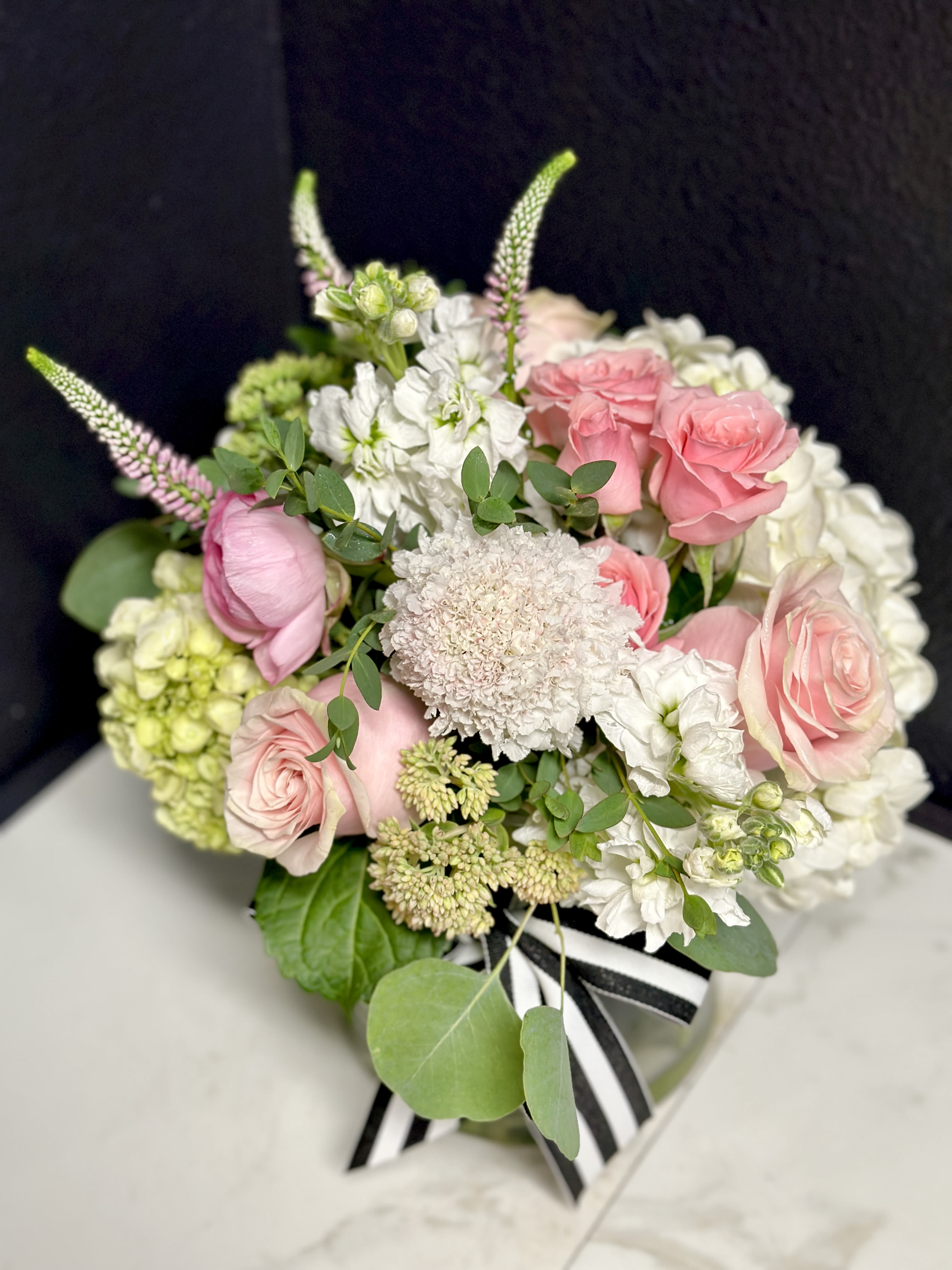 Pink and white bouquet with roses and hydrangeas tied with a striped ribbon