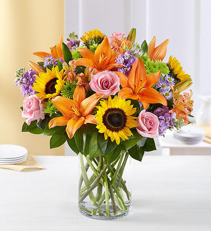 Garden of Grandeur - Luxurious and lasting. And able to transform any celebration into the must-attend gala of the season. A grand gathering of roses lilies sunflowers stock alstroemeria and more beautifully hand-arranged by our expert florists in a posh cylinder vase.