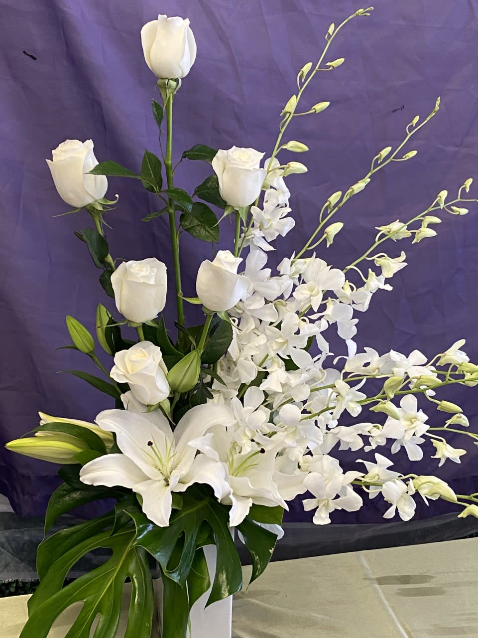 White roses, lilies, and orchids arranged in a tall vase