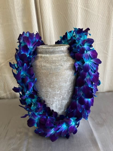 Purple and blue flower lei draped around a silver vase