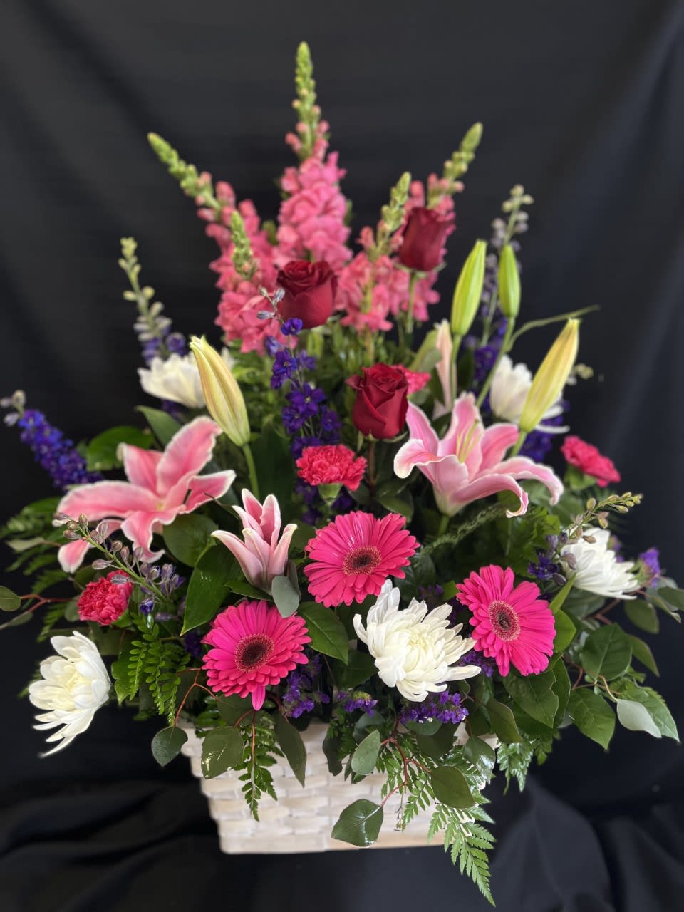 Mixed bouquet in a white basket with pink lilies, roses, and gerbera daisies