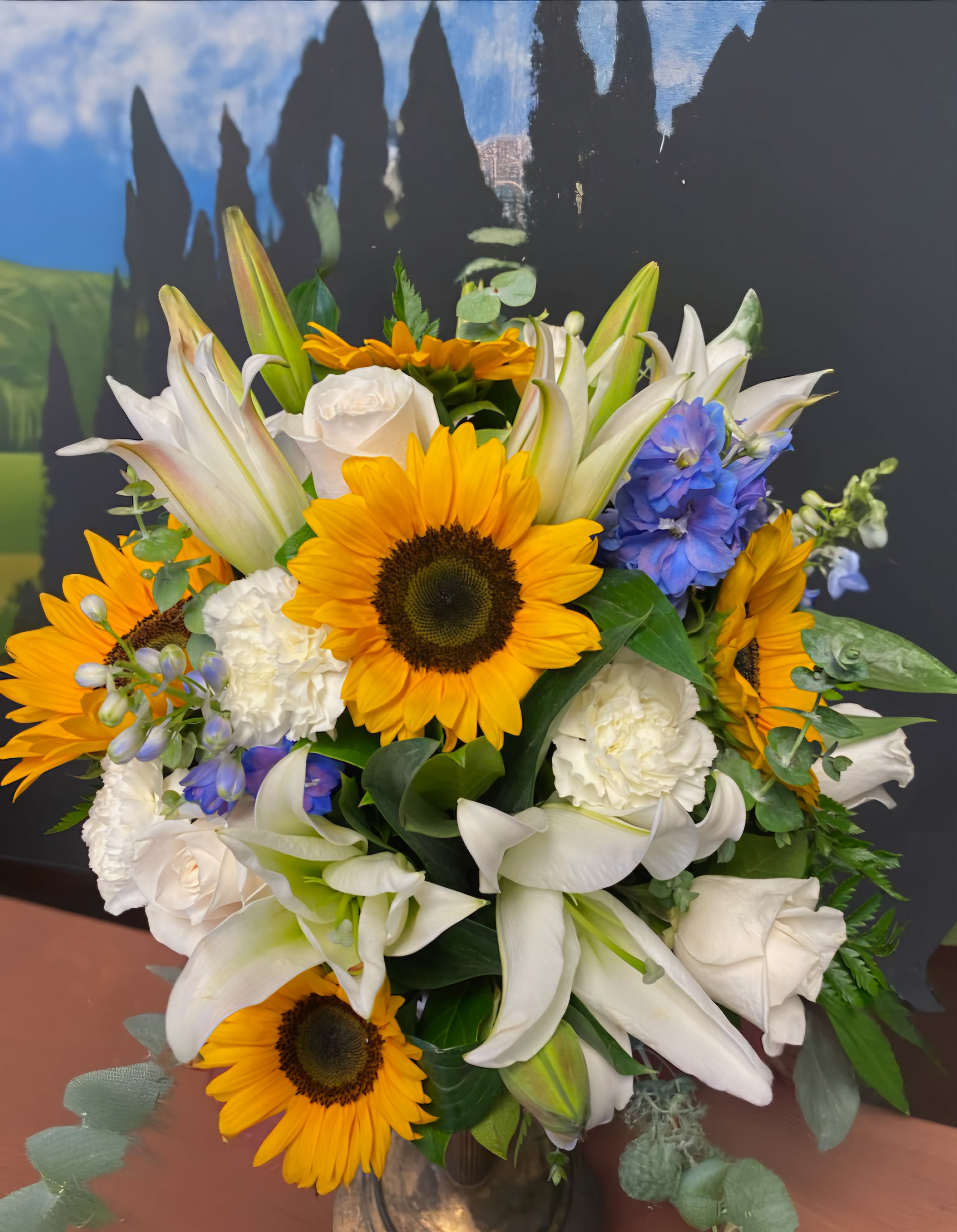 Bouquet of sunflowers, white lilies, and blue flowers in a vase