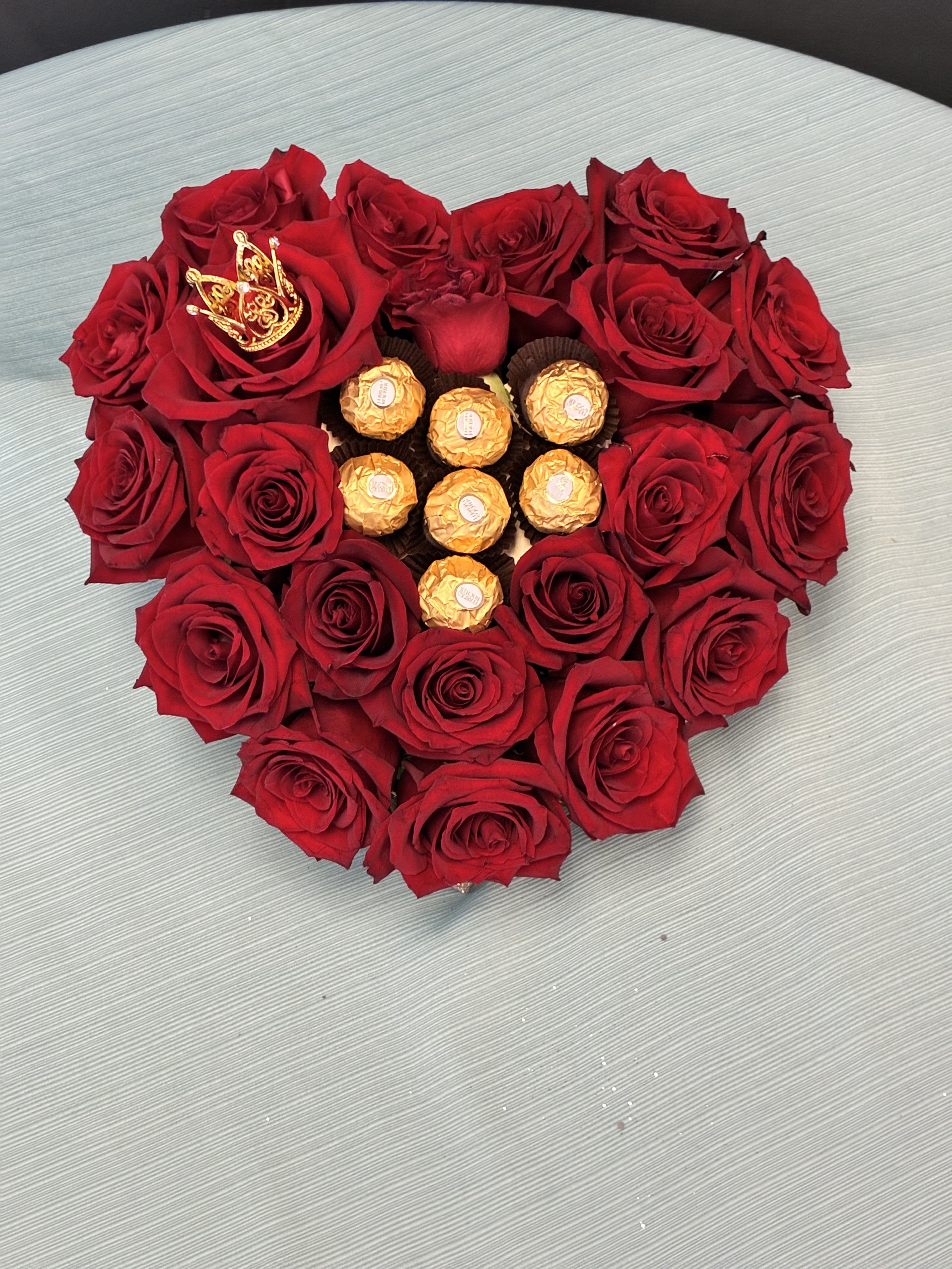 Heart-shaped red rose arrangement with gold-wrapped chocolates in the center