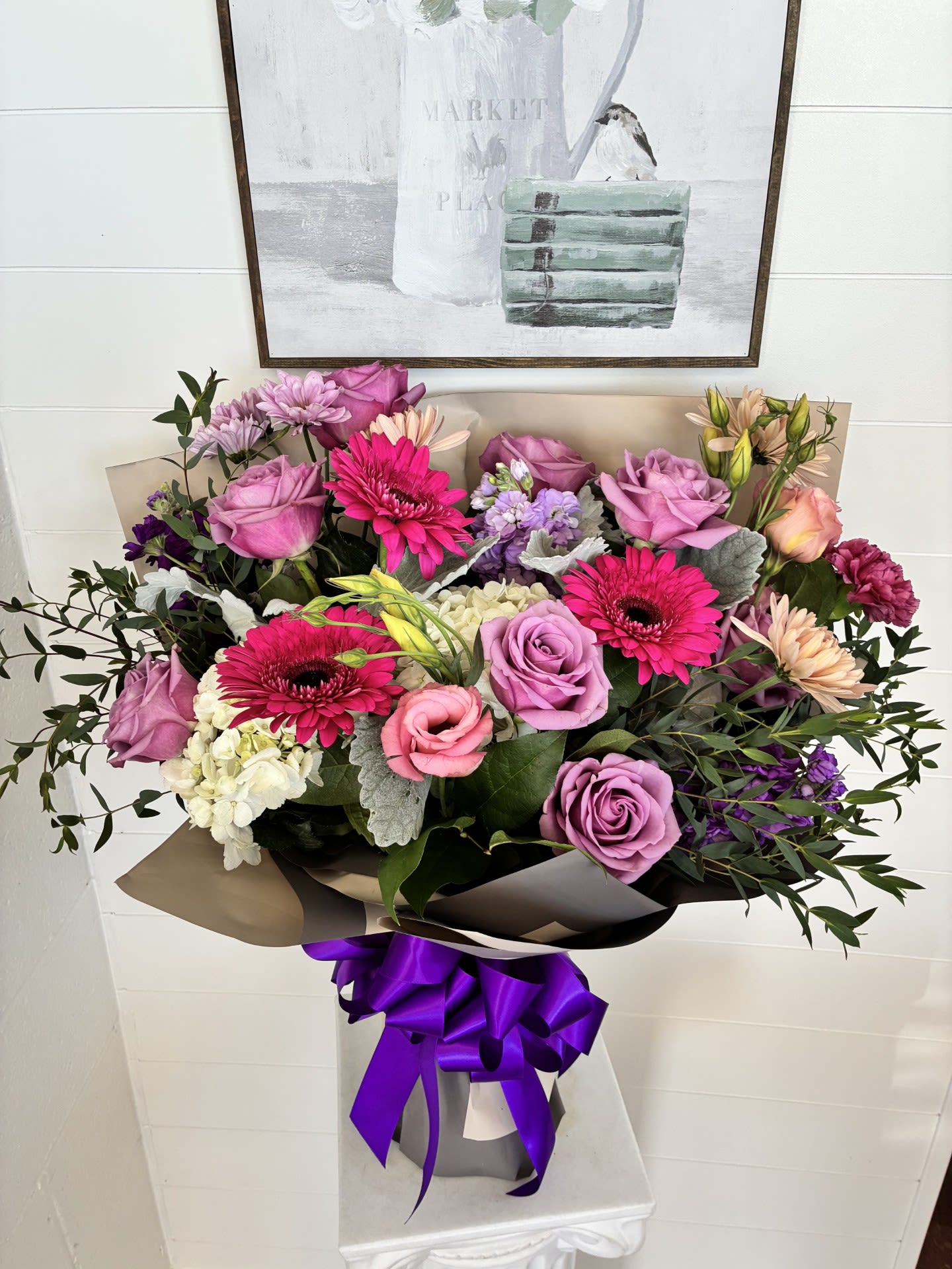 Blush of Summer - A cascade of soft pinks and lavender with pops of bright magenta-this blush summer bouquet feels like a warm, floral embrace. Perfect as a birthday bouquet, anniversary flowers, or an everyday thank-you arrangement, it's designed to make the person you're thinking of feel cherished and celebrated the moment they see it.  Roses, gerbera daisies, chrysanthemums, and alstroemeria are artfully arranged into a full, rounded bouquet with layers of small clustered blooms for rich texture and a romantic, soft look. The palette mixes pink, purple, white, and mixed tones with several vivid magenta gerbera daisies that draw the eye. Wrapped in neutral brown paper and tied with a vivid purple satin ribbon, the bouquet arrives ready to gift in a matching gift bag for easy presentation.  This arrangement suits recipients who appreciate classic romantic colors with a cheerful twist-moms, partners, friends, or coworkers marking a special day. Keep blooms in fresh, room-temperature water and away from direct heat; sizing and delivery options are available at checkout to ensure it arrives looking freshly gathered.