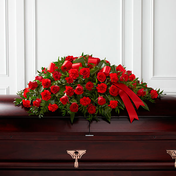 Red rose and carnation casket spray with ribbon on a dark casket
