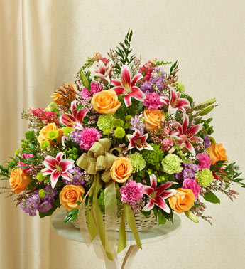 Basket arrangement of orange roses, pink lilies, and mixed blooms with a ribbon bow