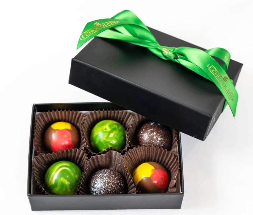 Black gift box of six colorful round chocolates with a green ribbon on the lid