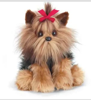 Small plush dog with long tan and black fur and a red bow on its head