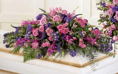Large pink and purple floral casket spray on a white casket