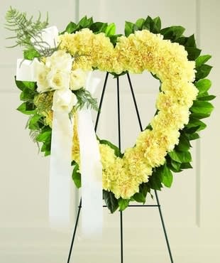 Heart-shaped yellow floral wreath on a stand with white ribbon