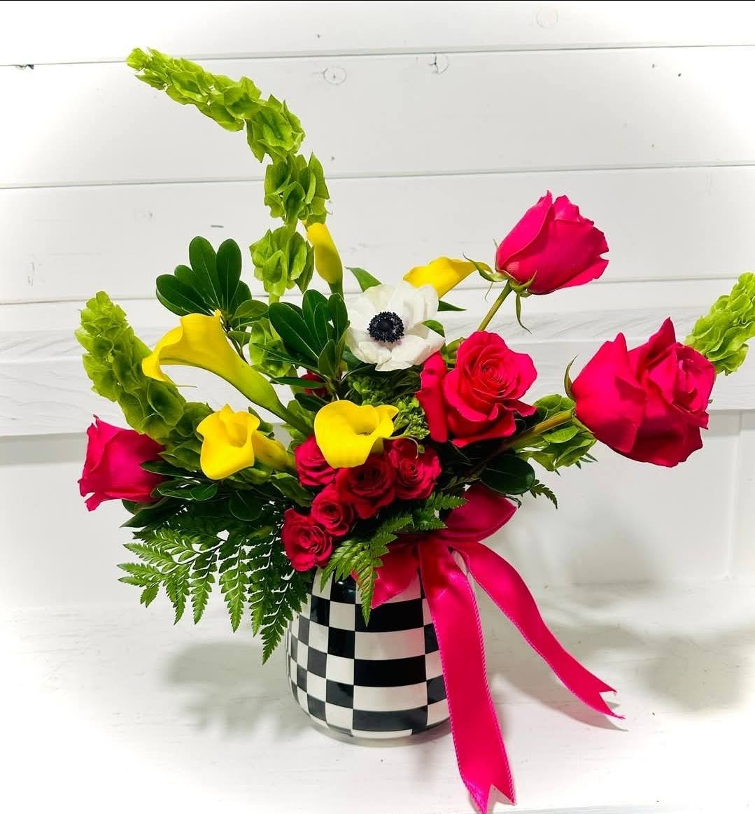 Bouquet of pink roses and yellow calla lilies in a checkered vase with a pink ribbon