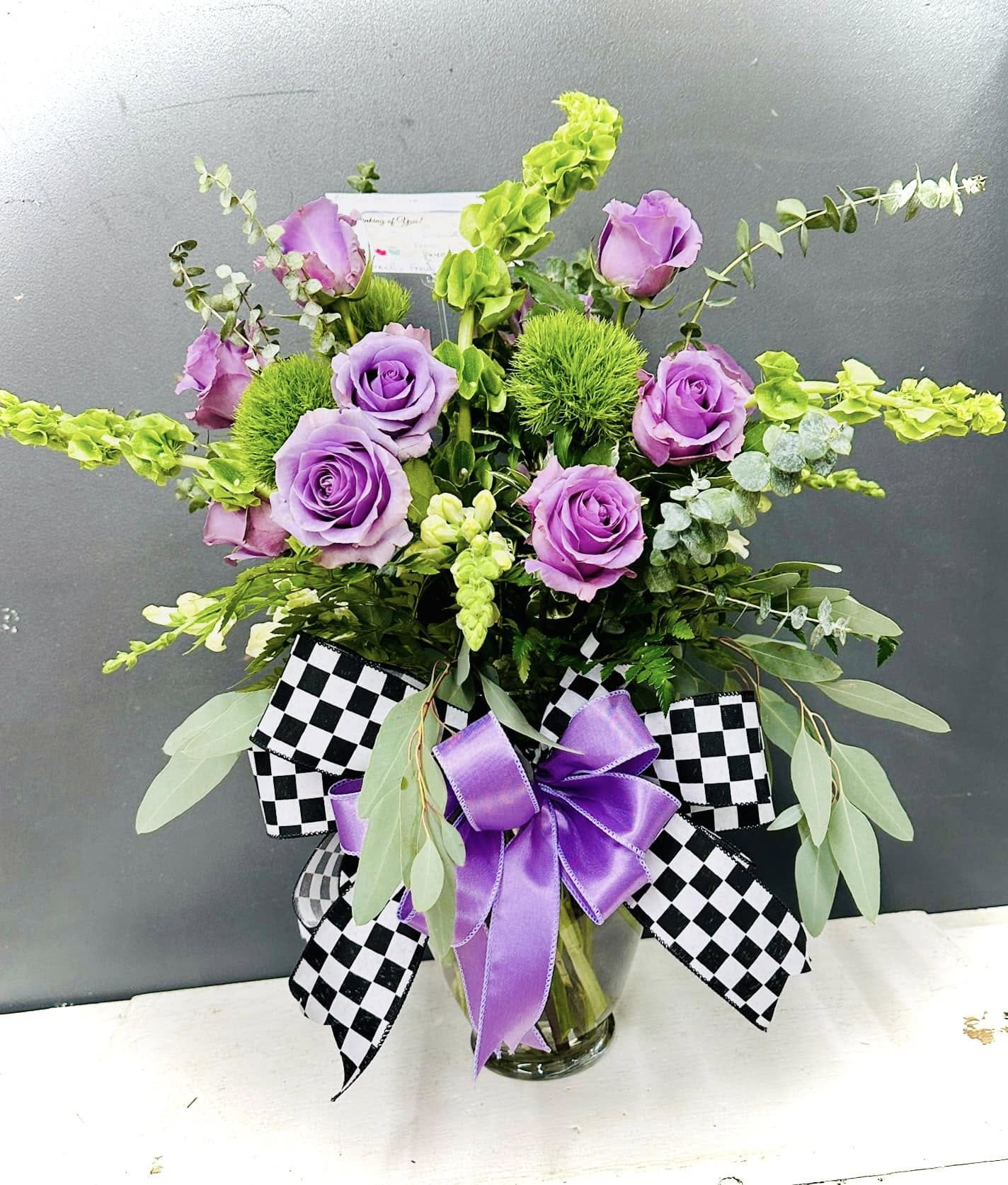 Purple roses in a glass vase with black-and-white checkered ribbon and a purple bow