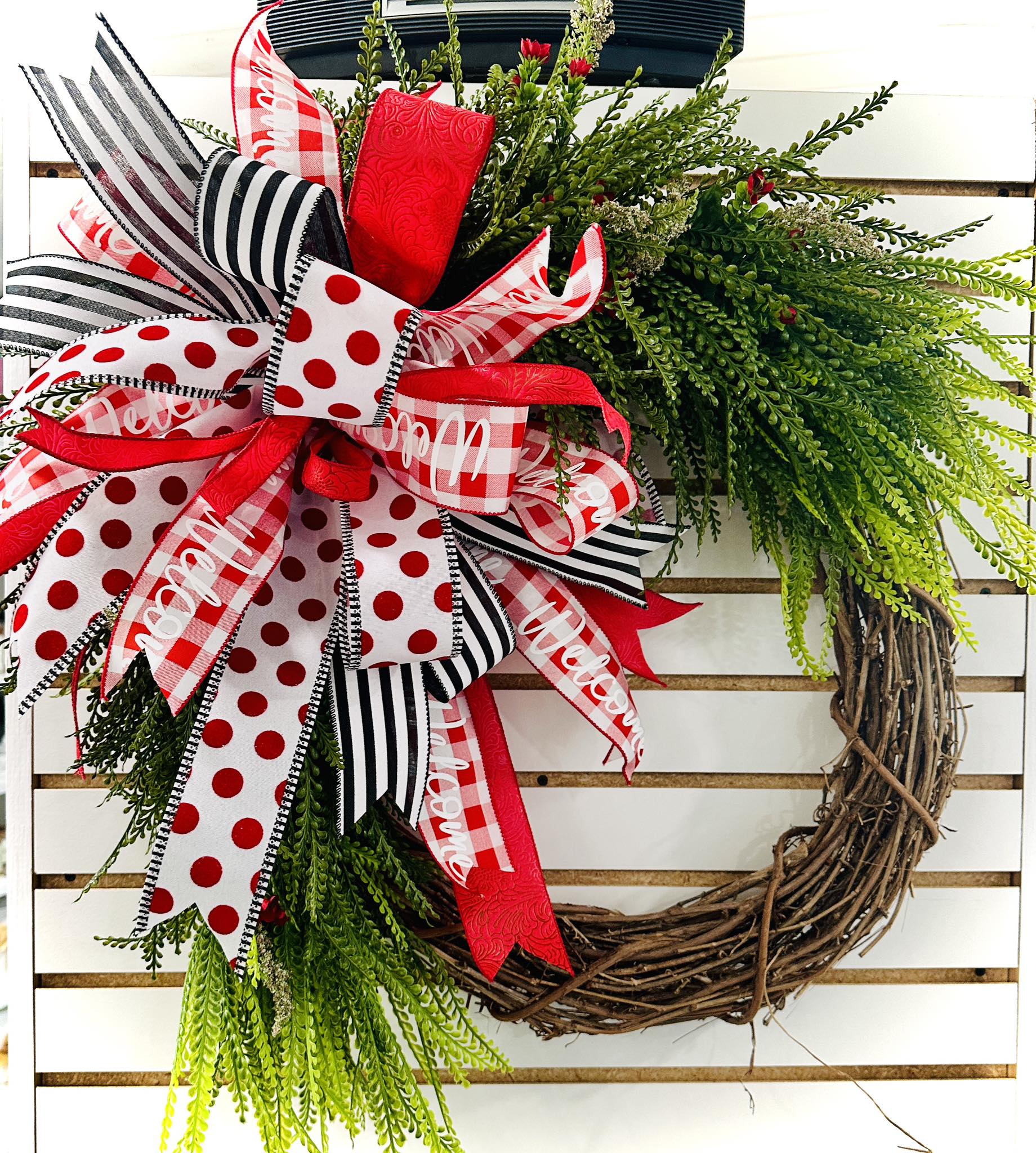 Decorative wreath with red, black, and white ribbons on a grapevine base