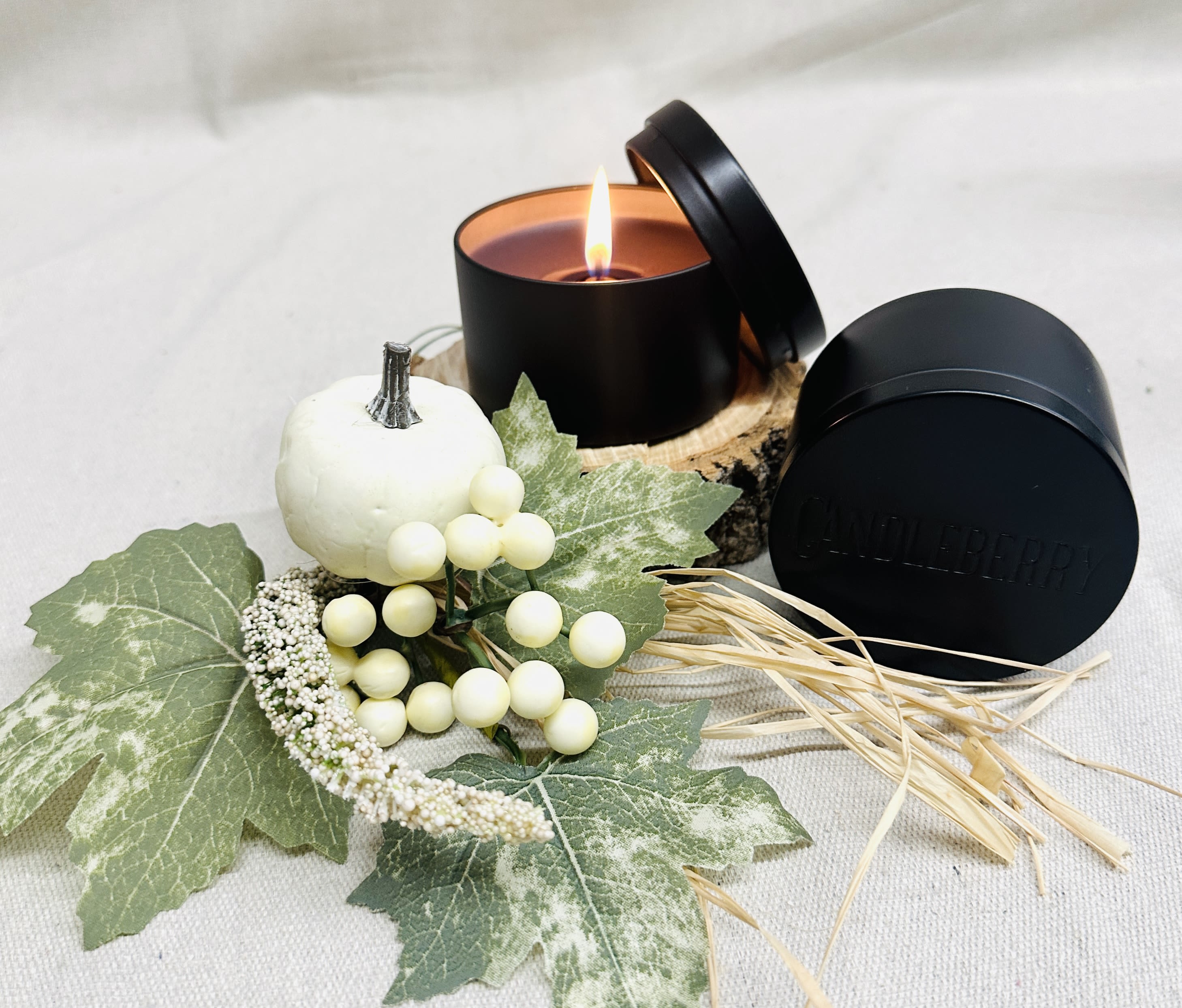 Black candle tin with a lit candle and autumn decor accents