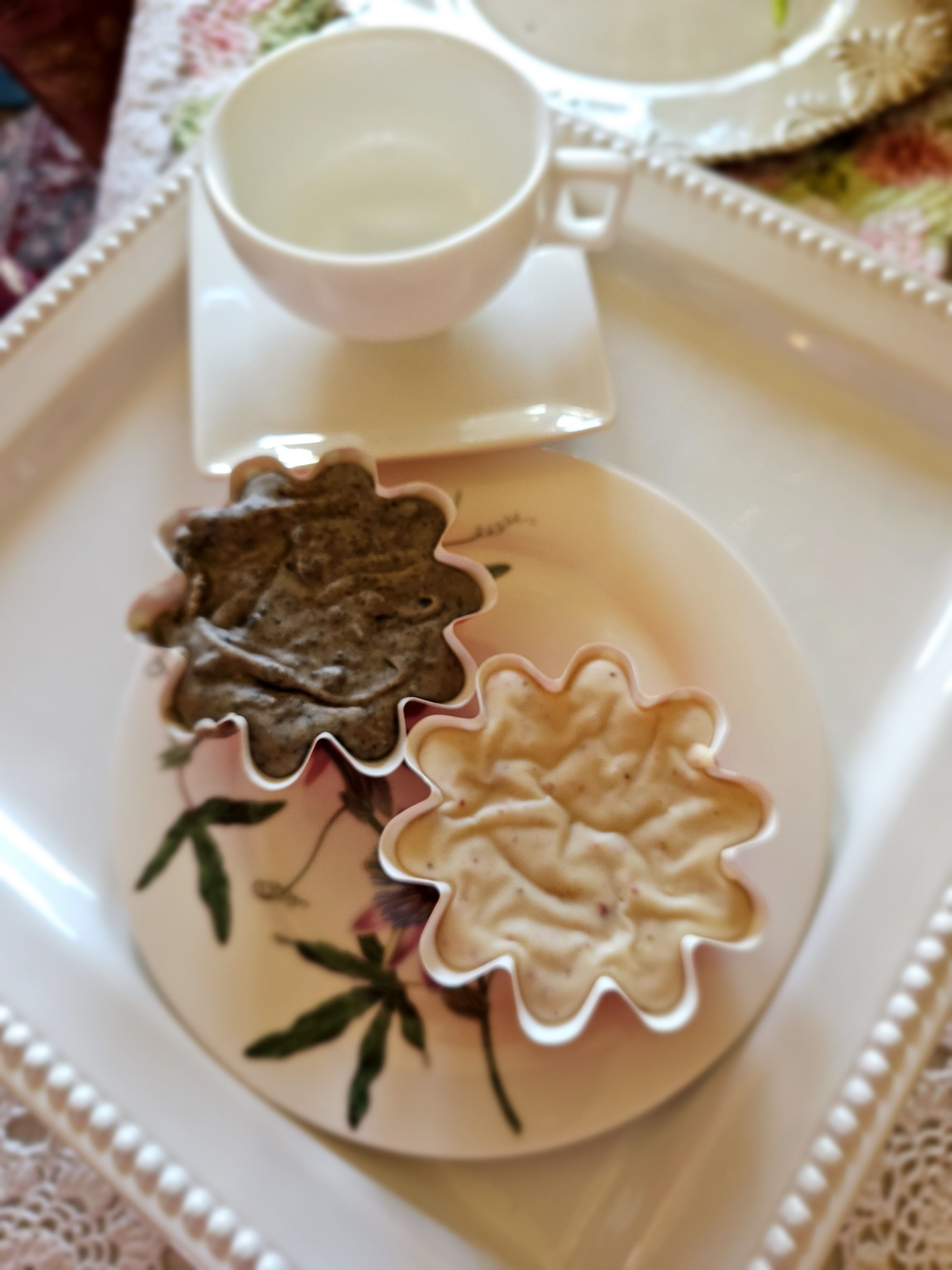 Two flower-shaped cups on a decorative tray with a square saucer.