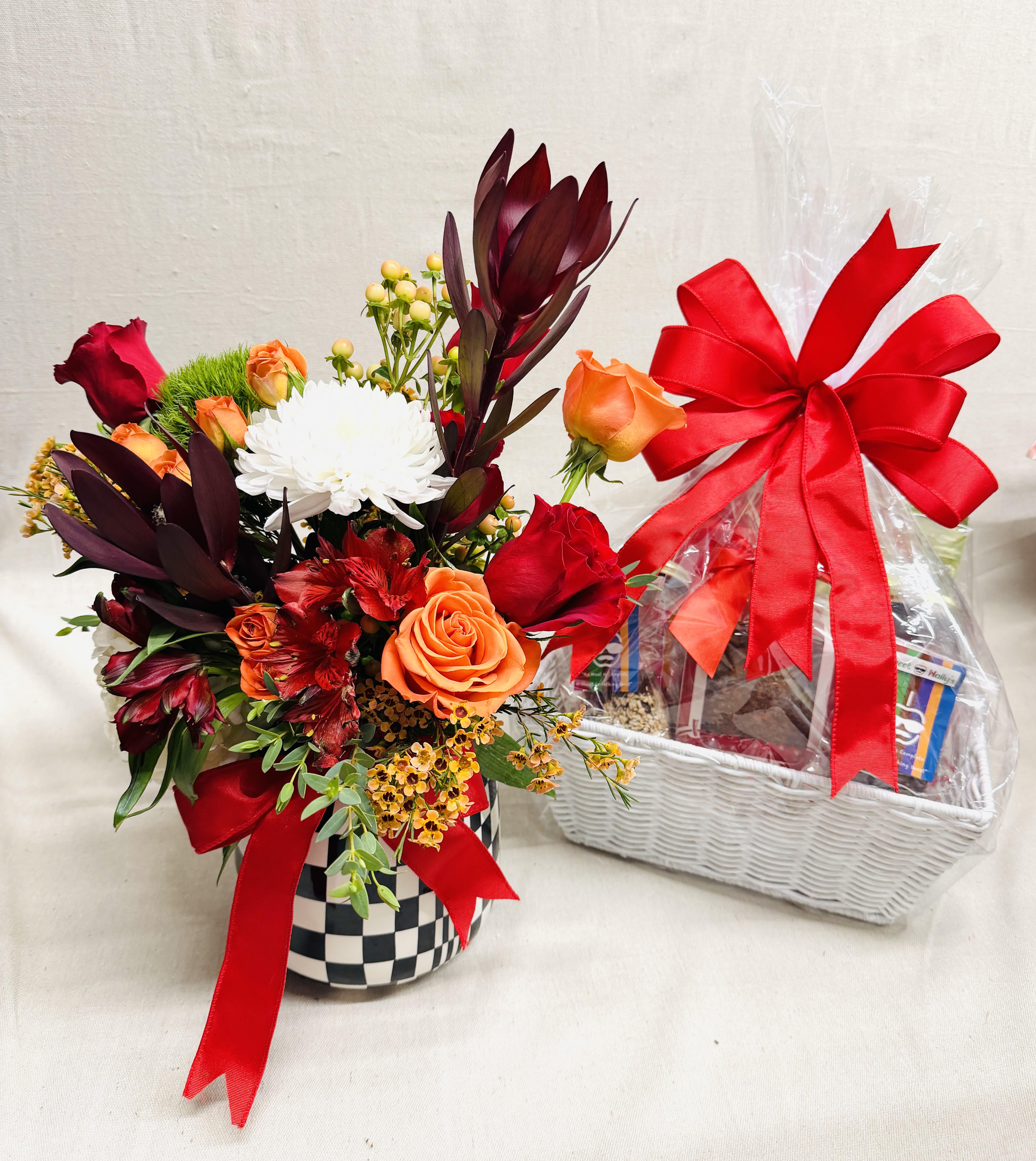 Mixed flower arrangement in a checkered vase beside a wrapped gift basket