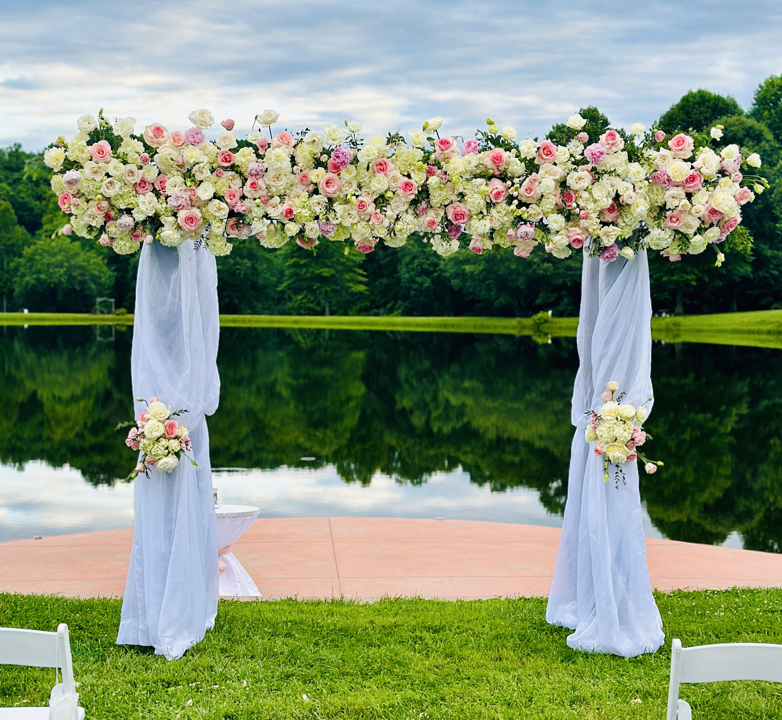 Floral wedding arch covered in pink and white roses with sheer white draping