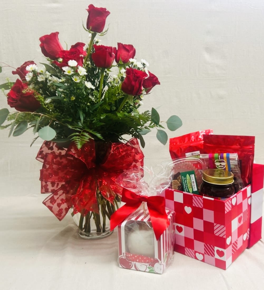 Red roses in a glass vase with a red ribbon, beside a Valentine gift basket