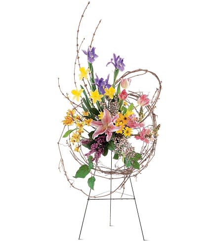 Tall floral standing arrangement with lilies, irises, and yellow blooms on a wire easel