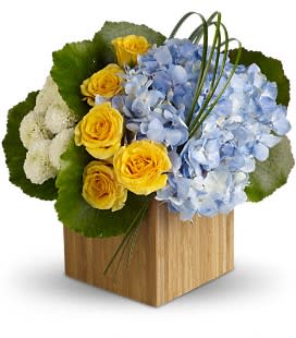 Yellow roses and blue hydrangeas in a wooden cube vase