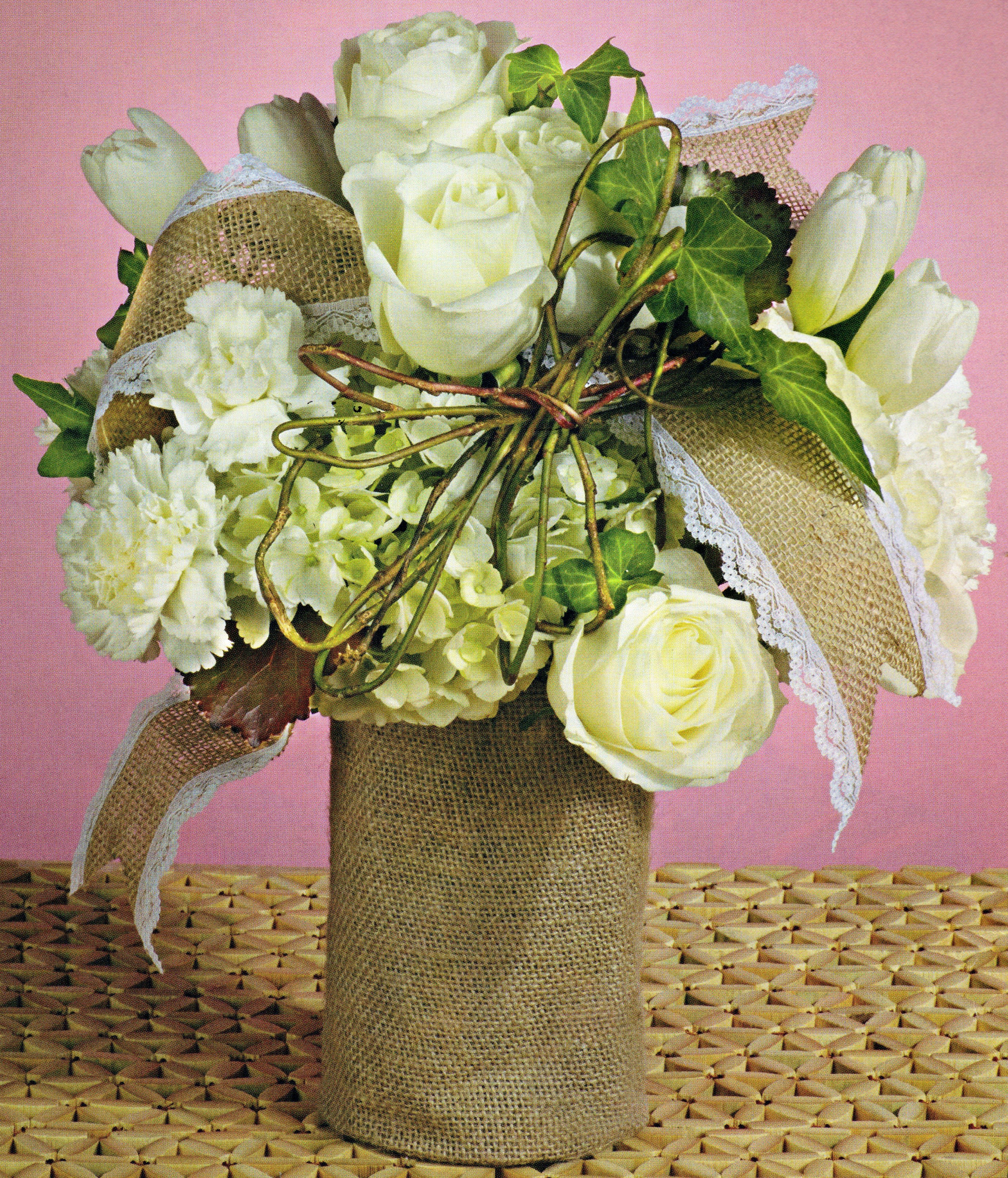 White roses and hydrangeas in a burlap-wrapped vase with lace ribbon