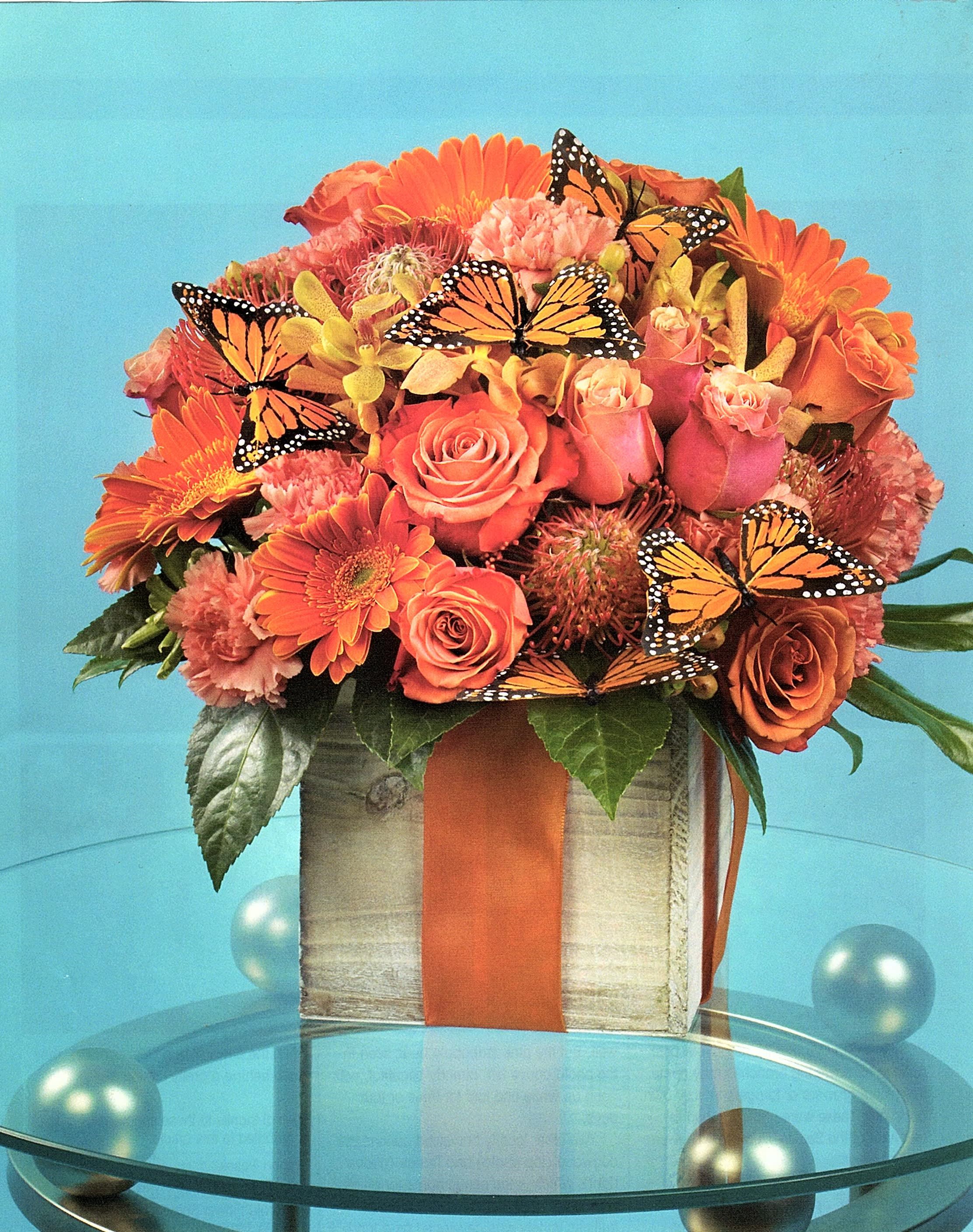 Orange and pink flower arrangement in a square box with butterfly accents