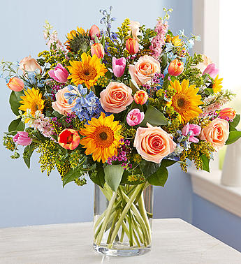 Mixed bouquet of roses, sunflowers, and tulips in a clear glass vase