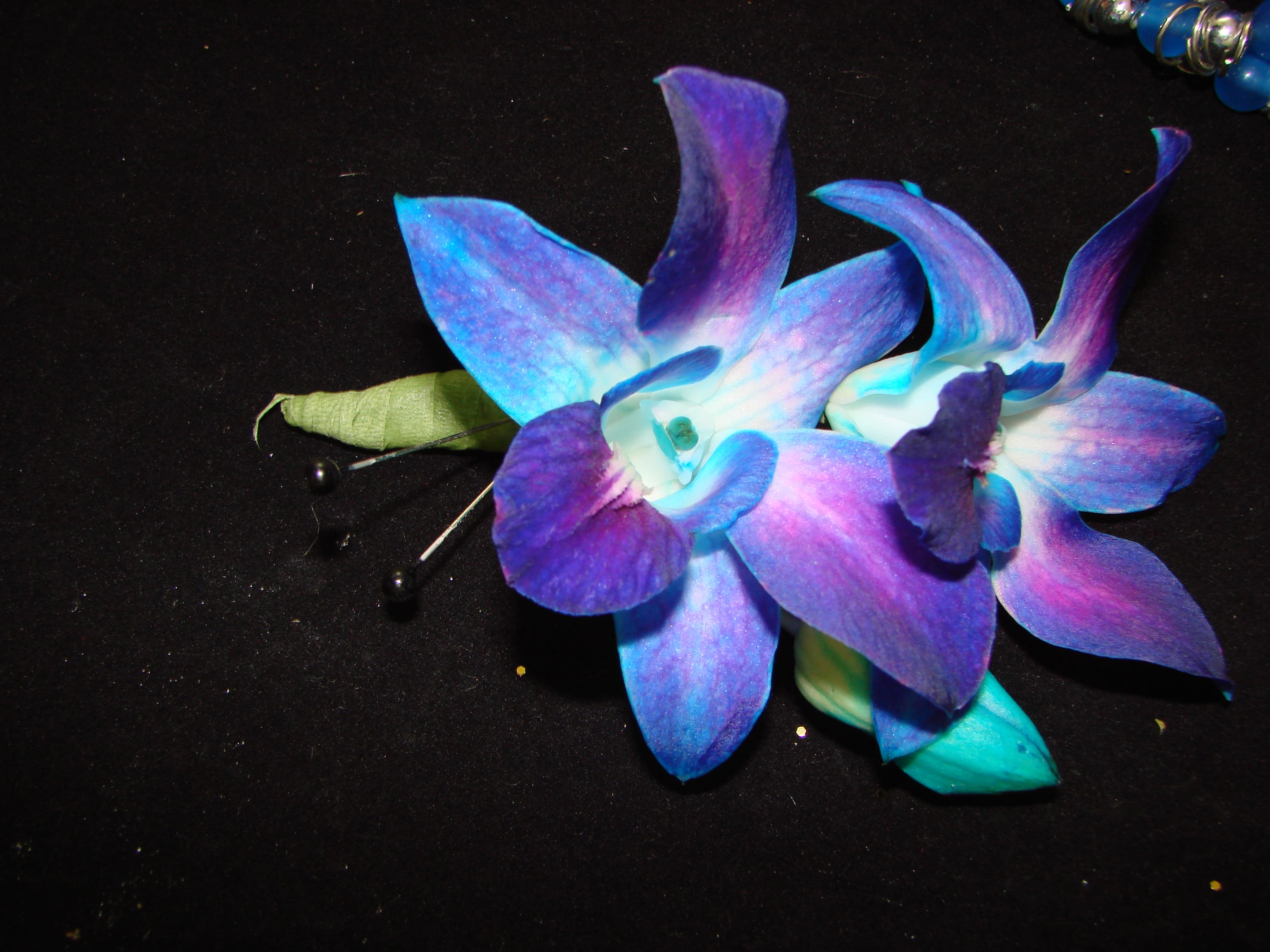 Two blue-purple orchid boutonnieres on a dark surface
