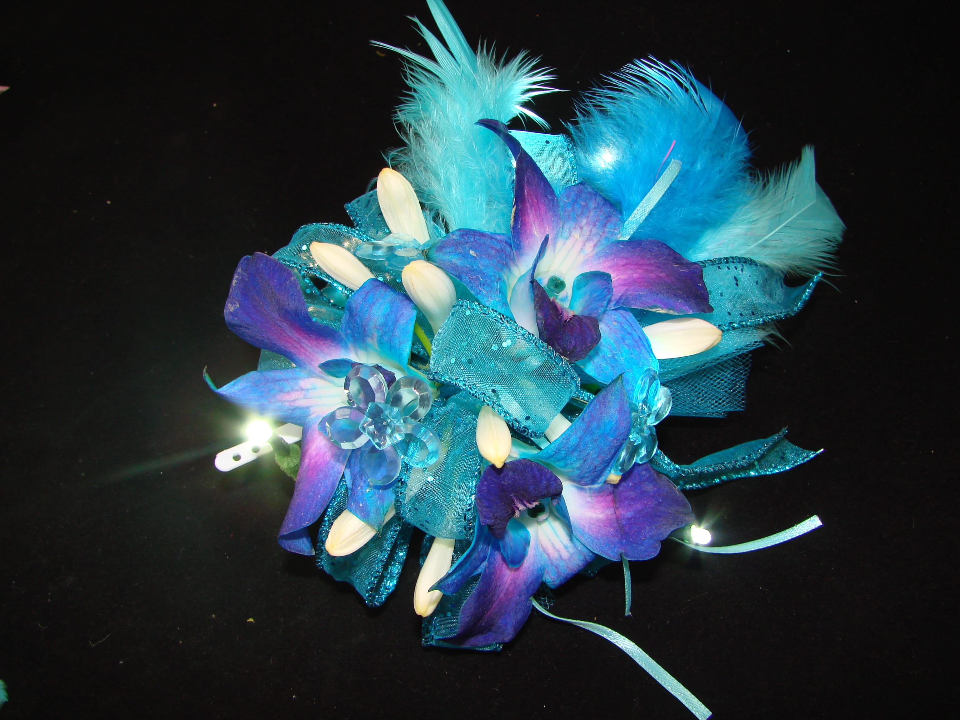 Blue and purple floral corsage with feathers and ribbon on a black background