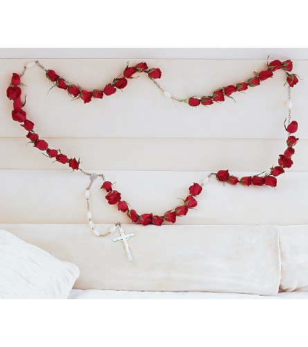 Red rose garland draped across a white couch with a hanging cross