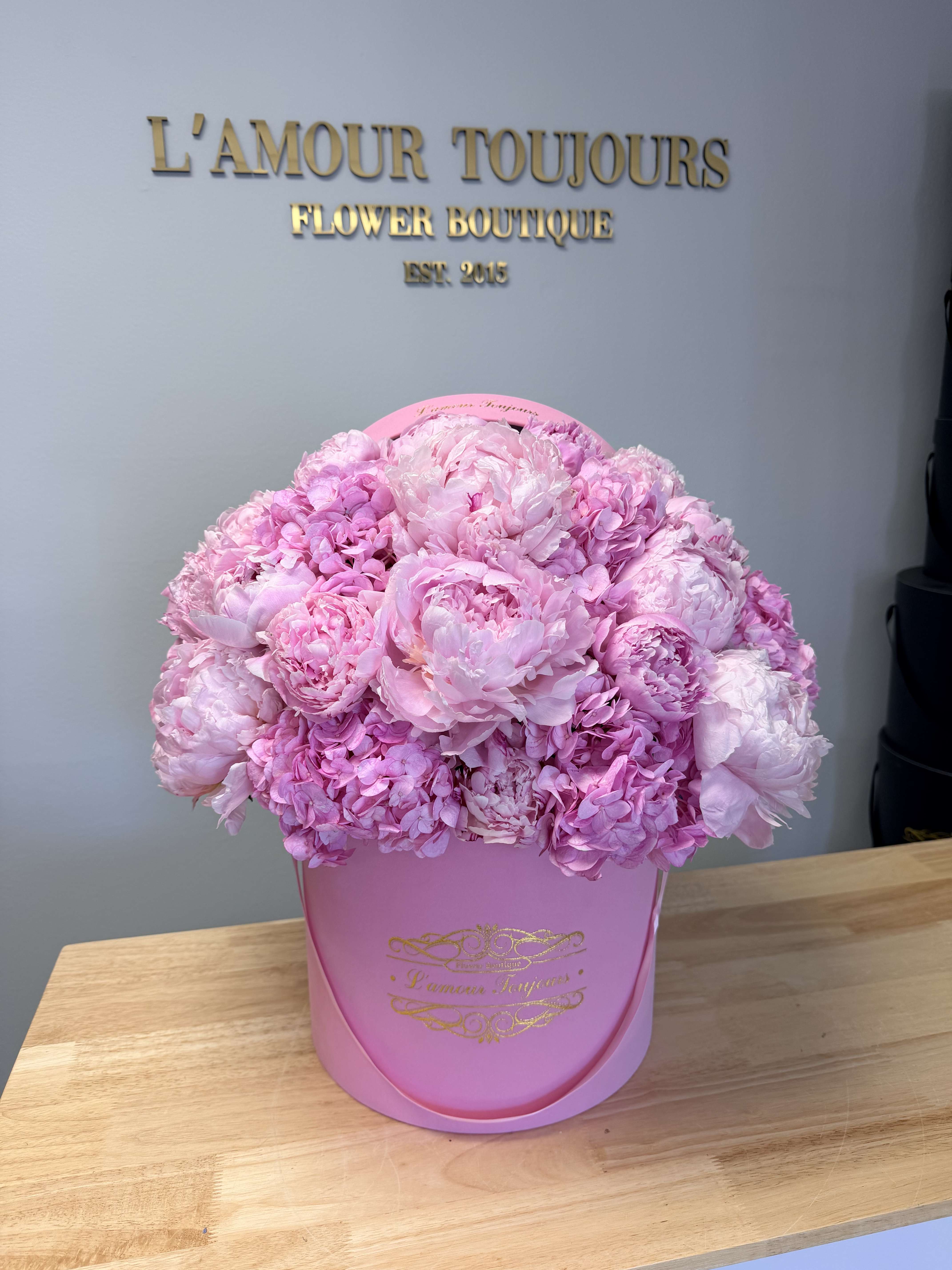 Pink peonies and hydrangeas arranged in a pink hat box