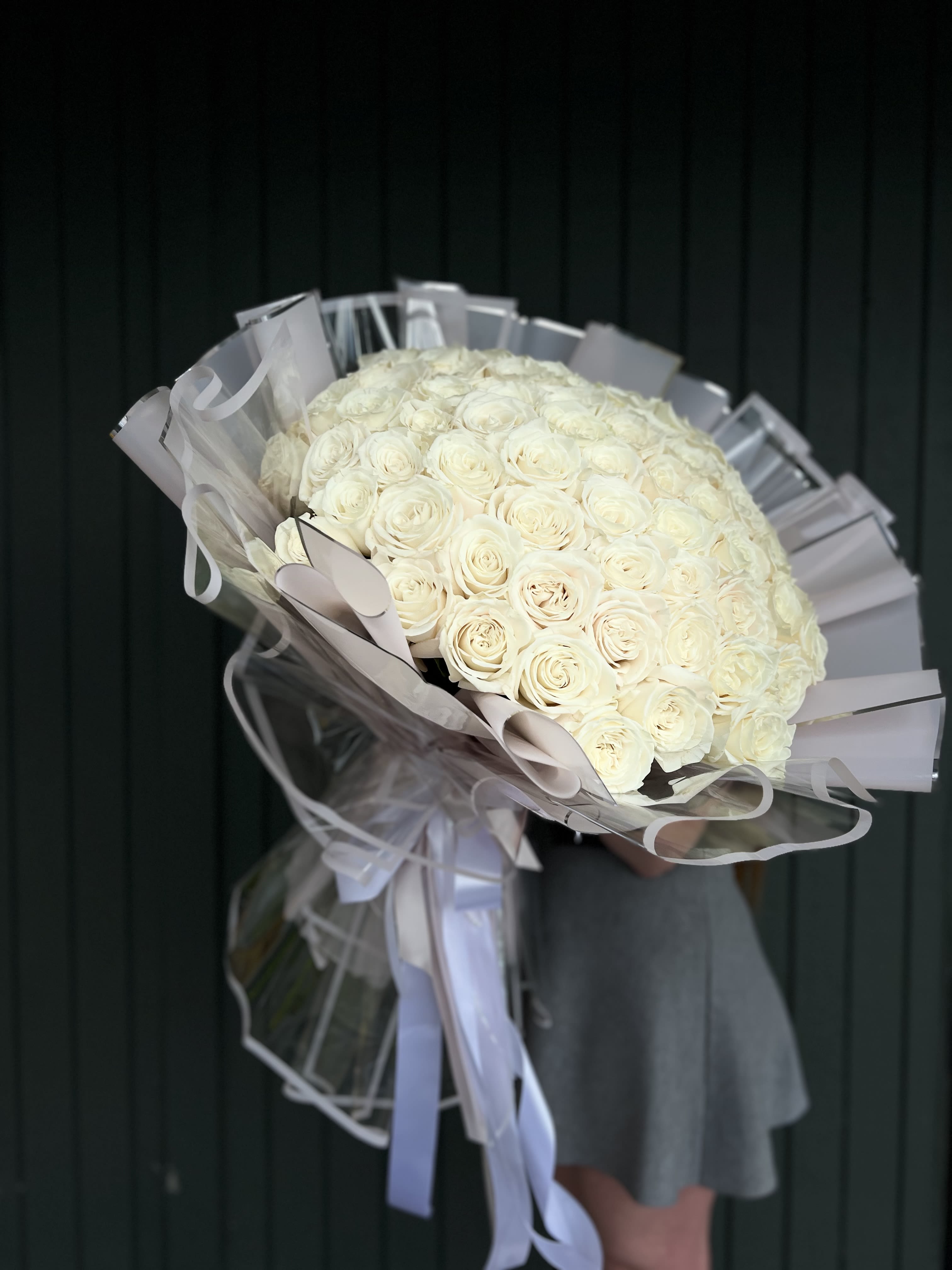 Large bouquet of white roses wrapped in clear plastic with ribbon