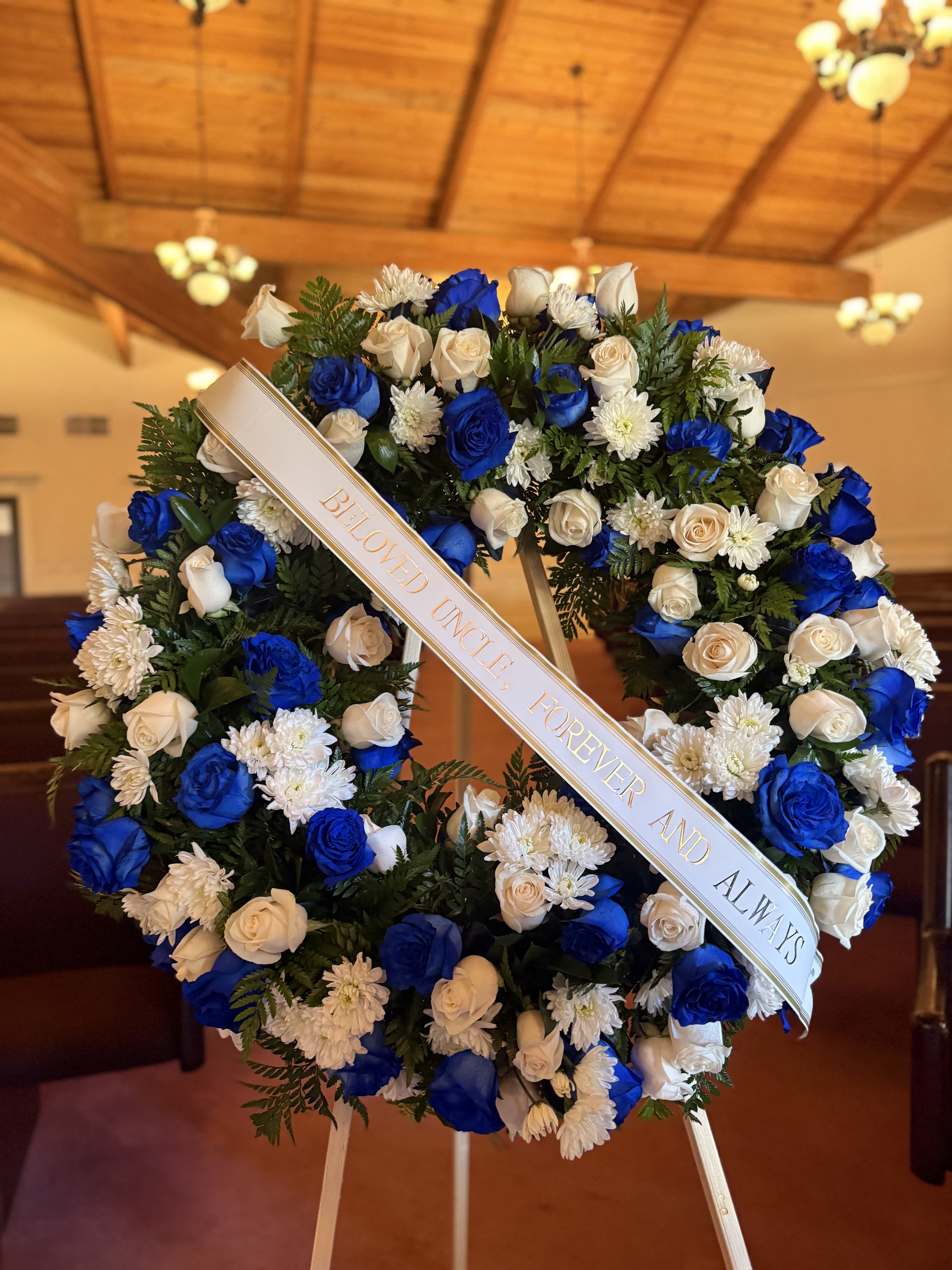 Blue and white floral funeral wreath with a memorial ribbon on an easel