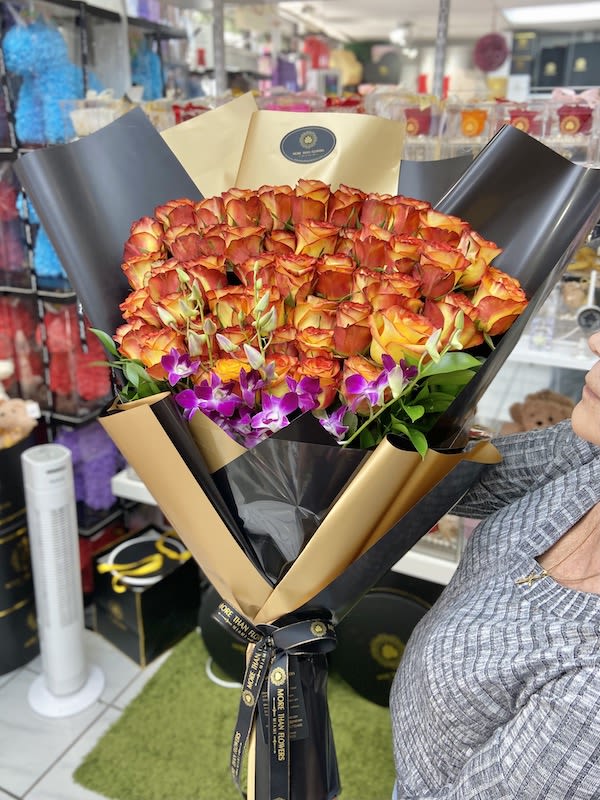 Large bouquet of orange roses with purple orchids wrapped in black and gold paper