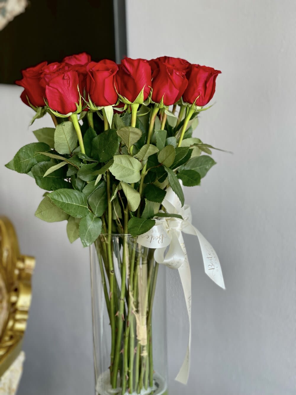Tall bouquet of red roses in a clear glass vase with a white ribbon
