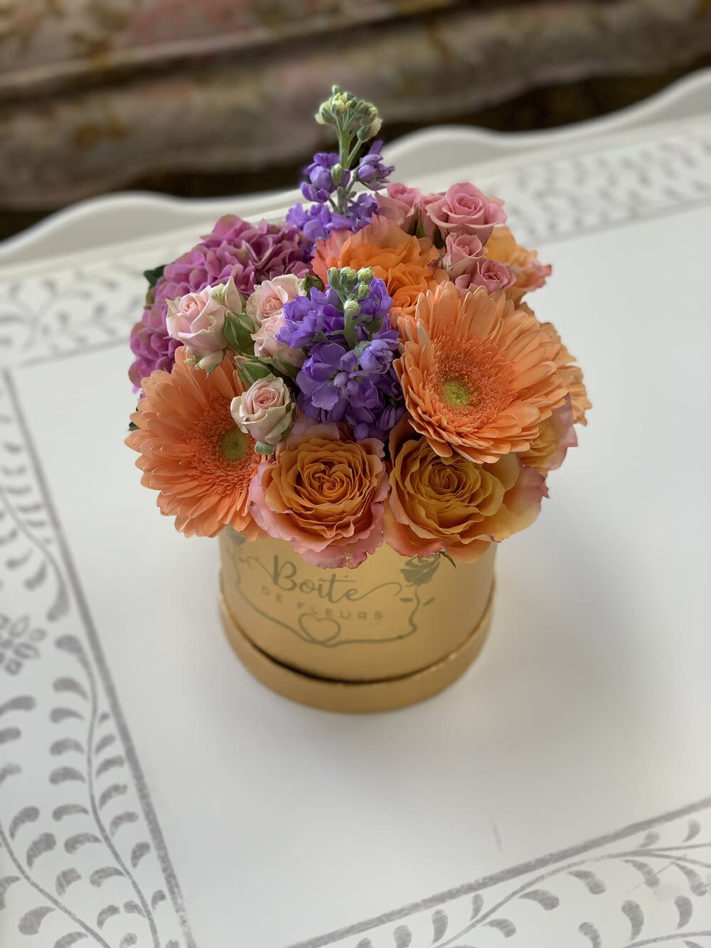 Bouquet of orange gerberas, pink roses, and purple flowers in a gold box