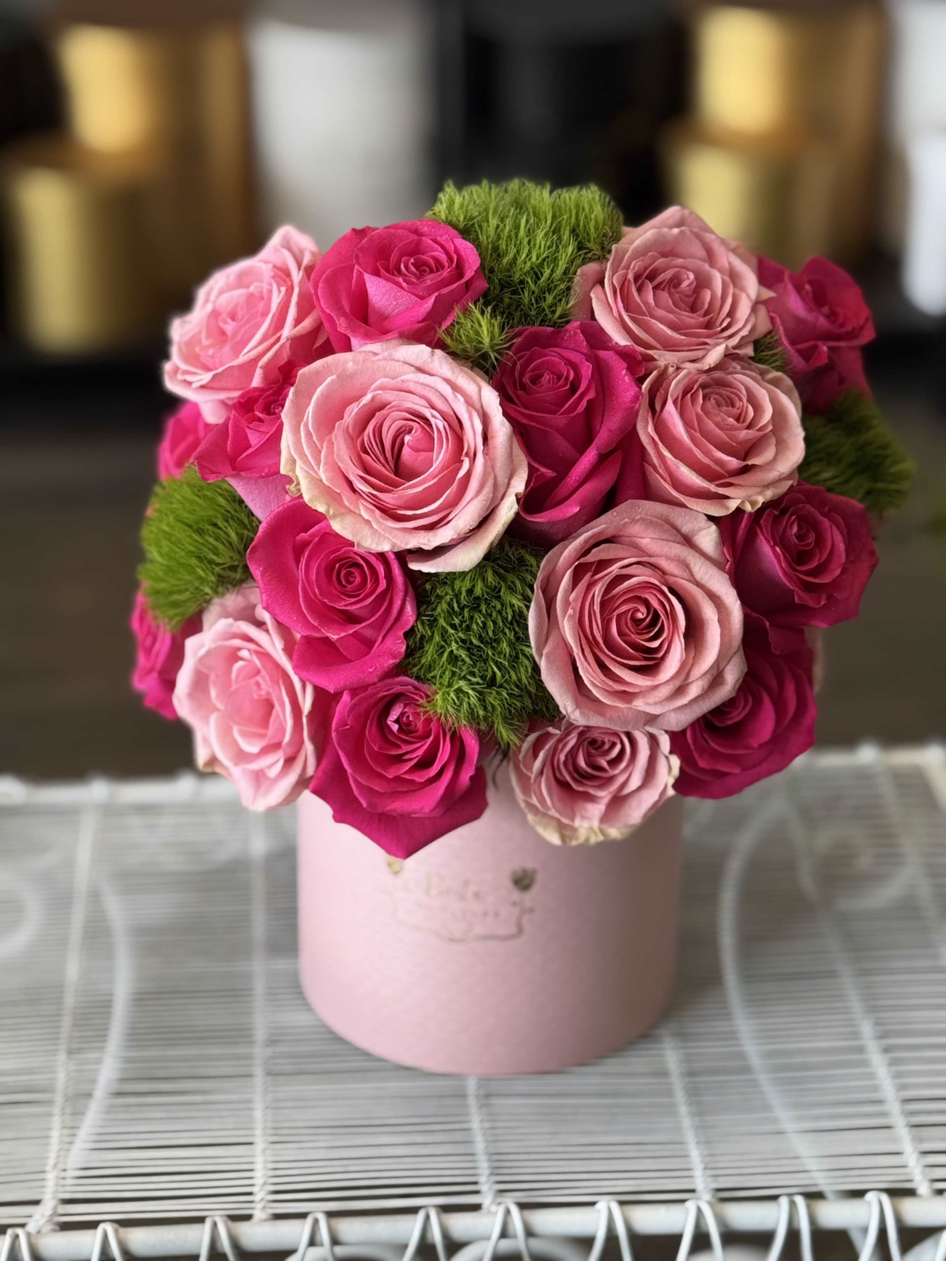 Pink and hot pink roses arranged in a round box with green moss accents