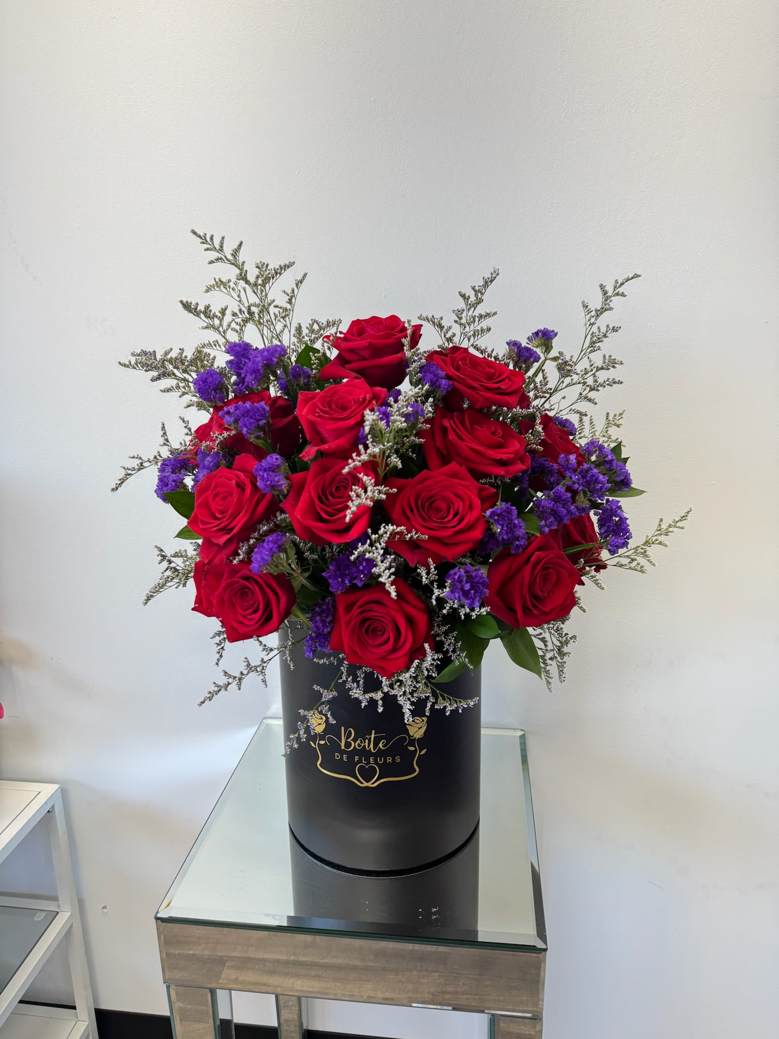 Red roses and purple filler flowers in a black hatbox