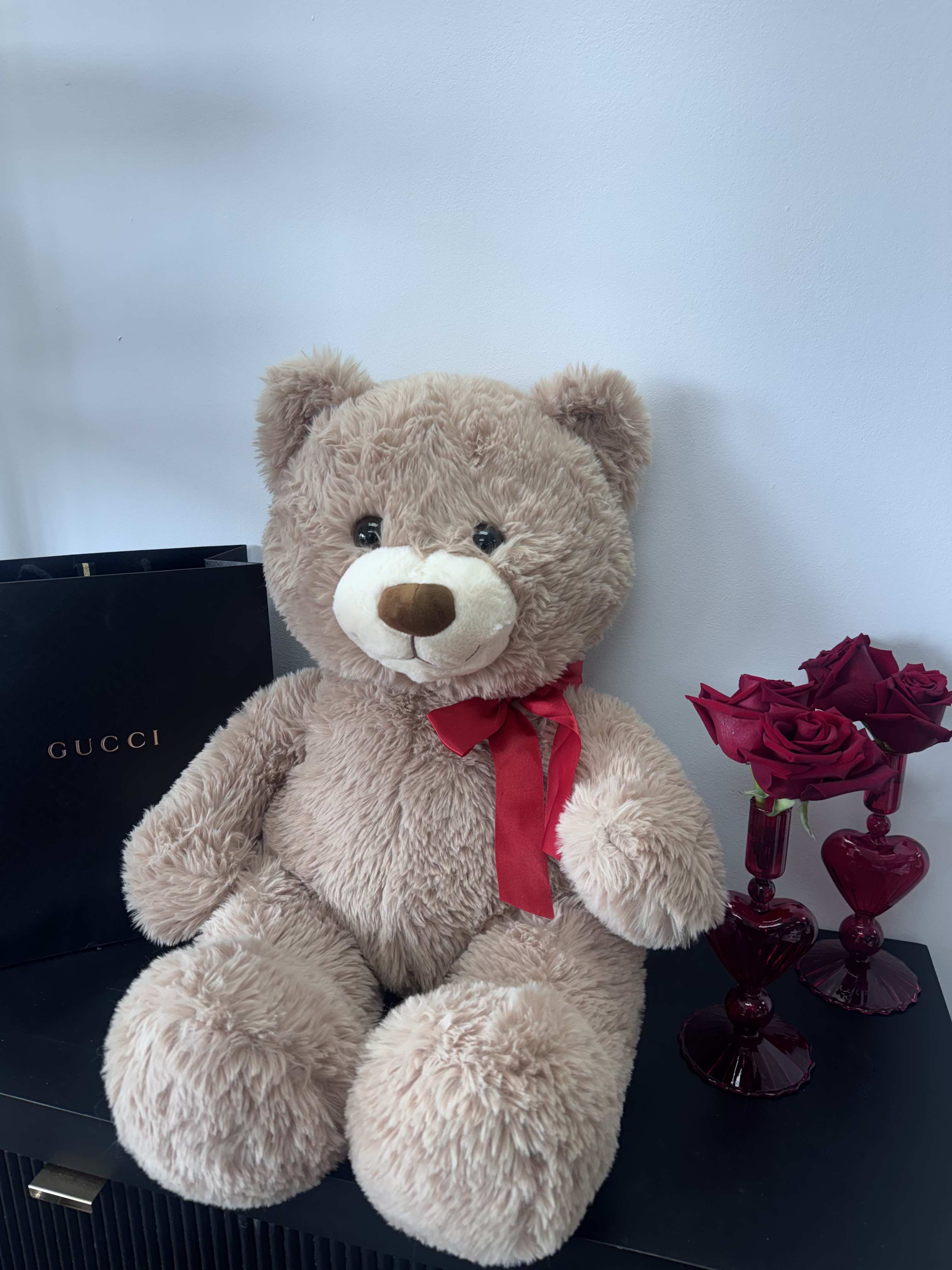 Teddy bear with a red ribbon beside a small vase of red roses