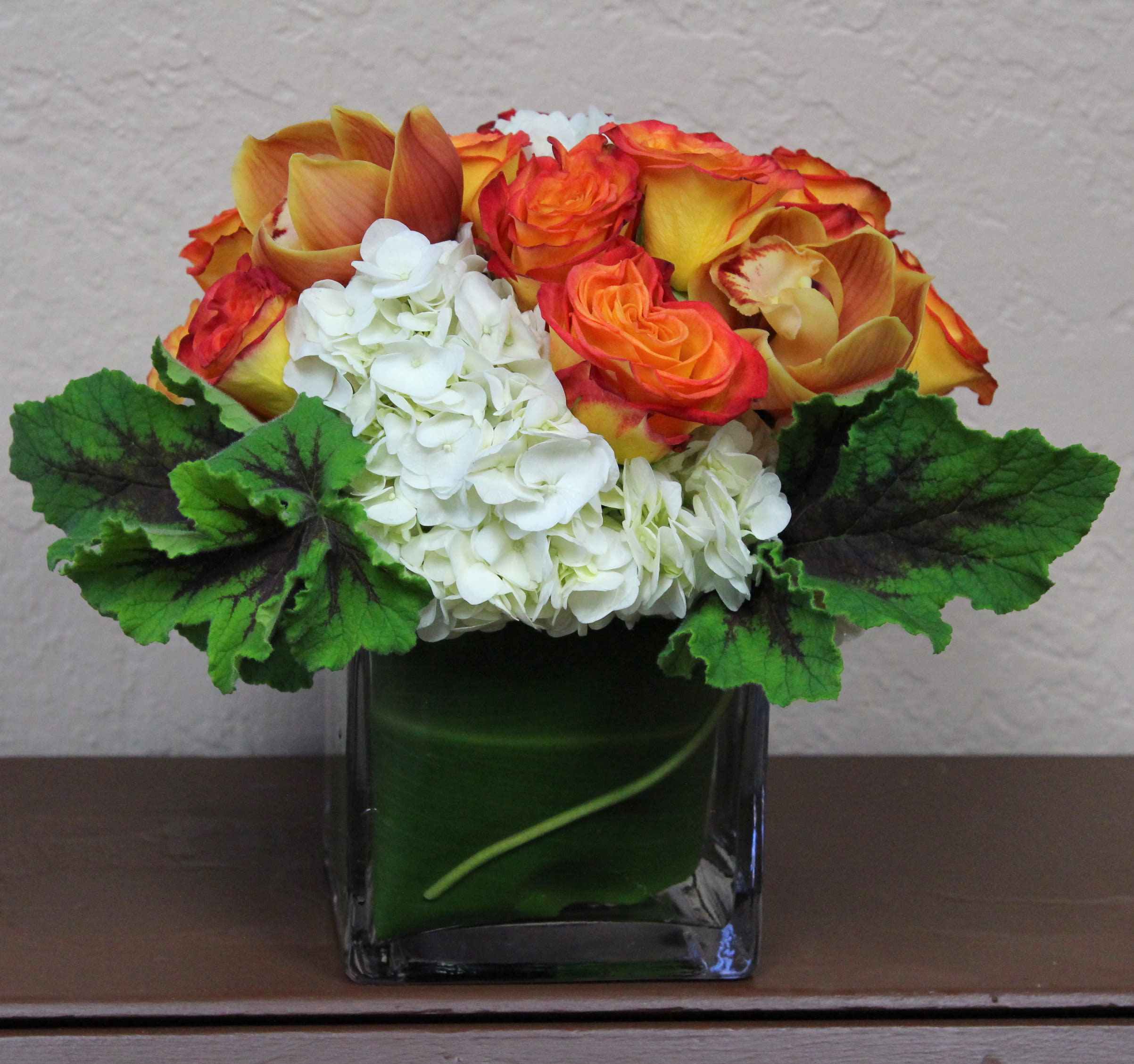 Orange roses and white hydrangeas in a square glass vase