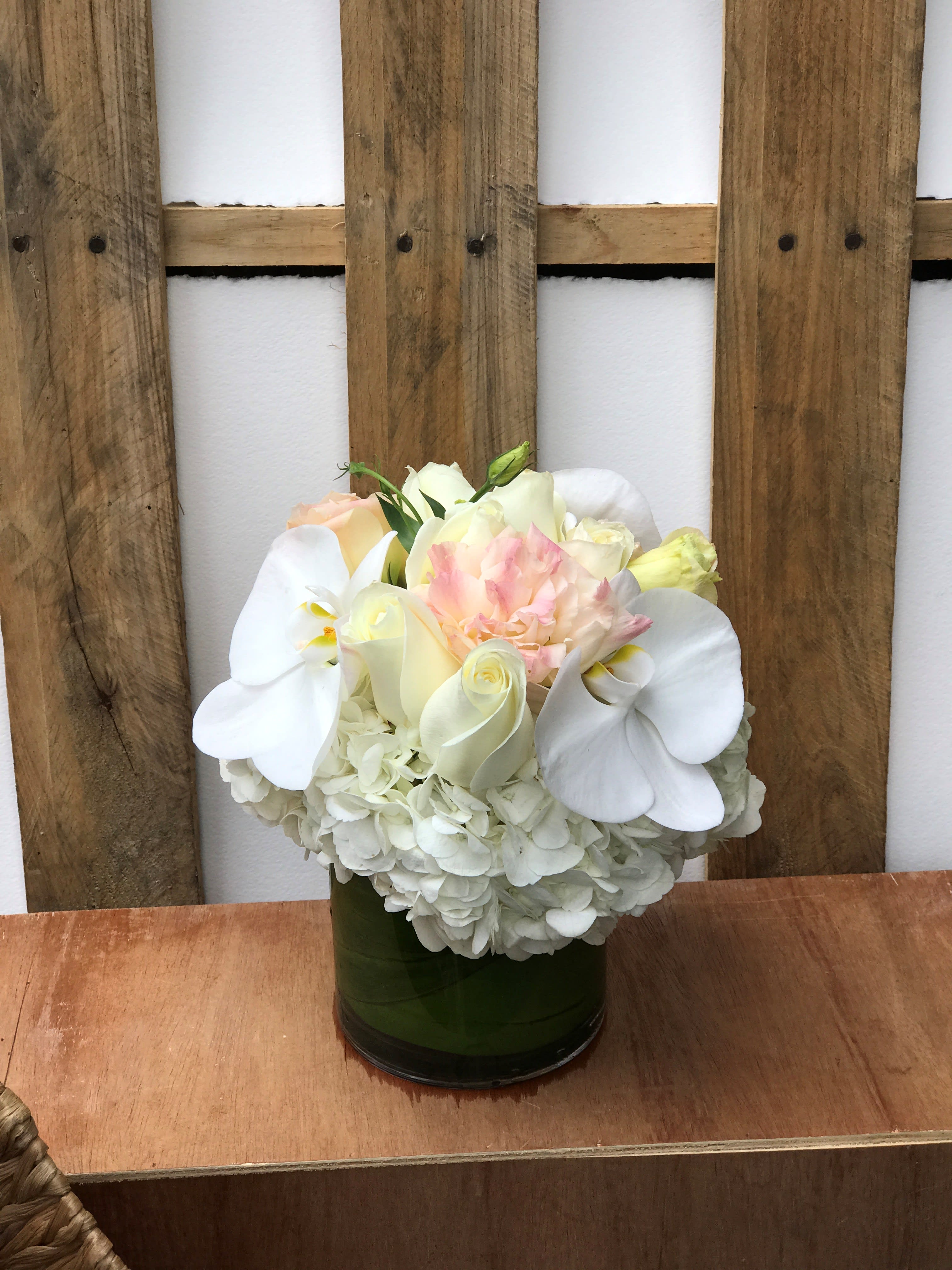 White and blush floral arrangement in a green glass vase