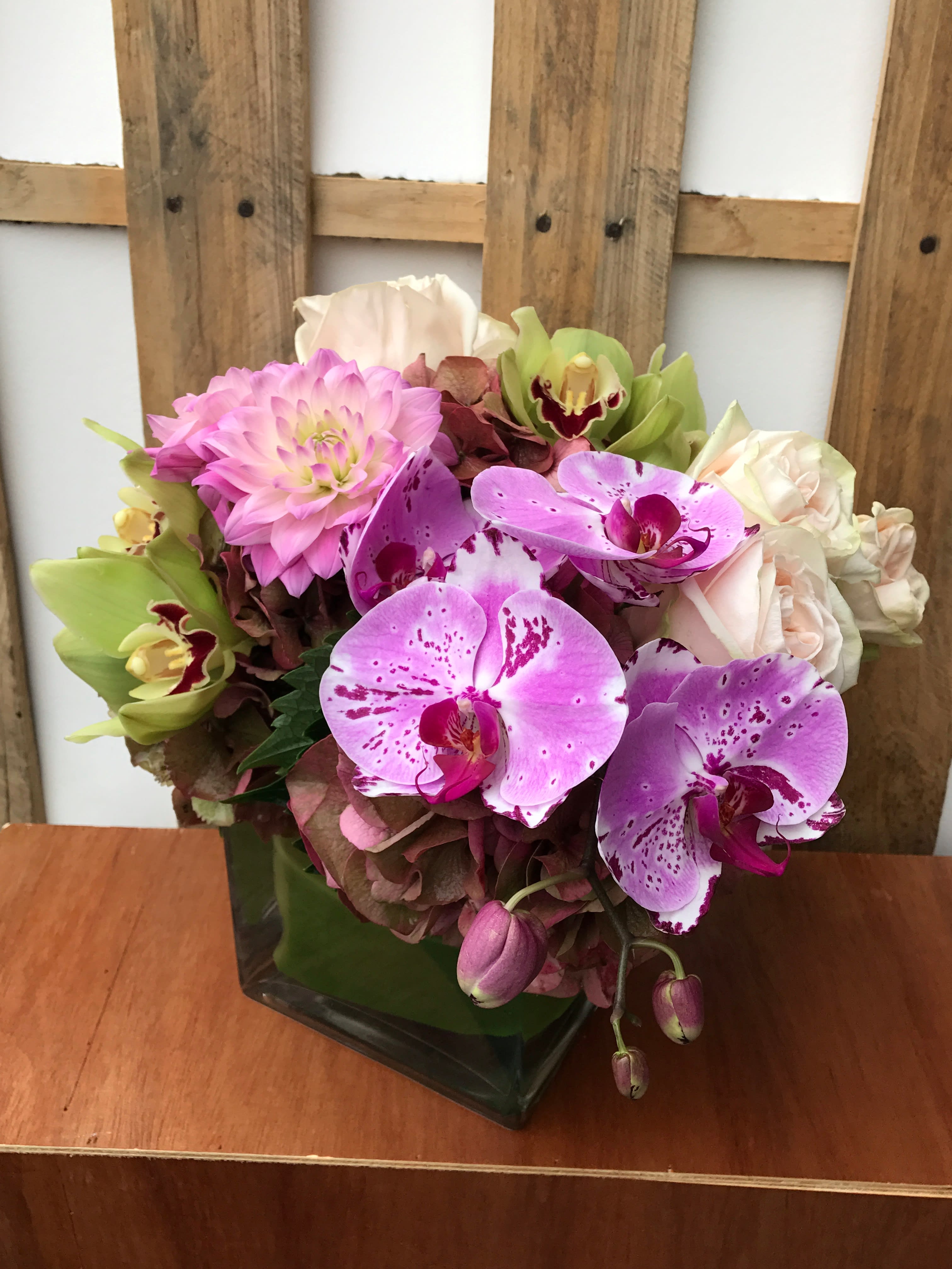 Pink and purple orchid arrangement in a square glass vase