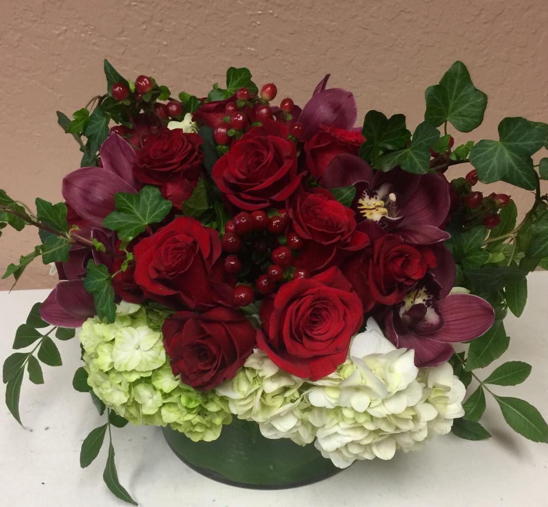Red roses and purple orchids arranged with hydrangeas in a green container